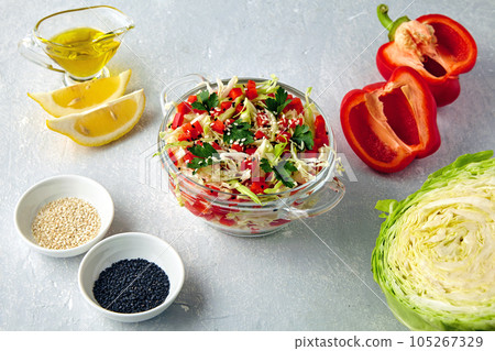 Fresh summer light salad of young white cabbage with bell peppers, parsley and sesame seeds surrounded by ingredients on light concrete table Fresh summer light salad of young white cabbage with bell peppers, parsley and sesame seeds surrounded by ingredients on light concrete table 105267329