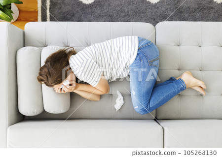 Frustrated woman covering face and crying, lying on sofa at home alone 105268130