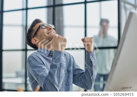 Excited modern businessman sitting at office desk and rejoicing his success 105269455