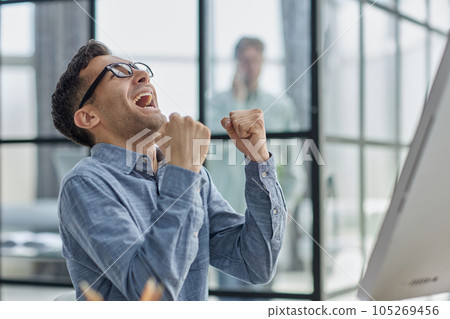 Excited modern businessman sitting at office desk and rejoicing his success 105269456