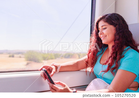Train traveler. Hispanic mid-adult woman looking smartphone on holiday lifestyle vacation Train traveler. Hispanic mid-adult woman looking smartphone on holiday lifestyle vacation 105270520
