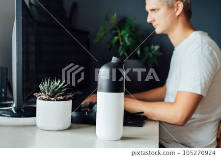 Focus on shaker with dry dehydrated meal on the desk of young man working on pc. IT specialist programmer eating during work. Balanced nutritionally complete meals diet. Food replacement. Biohacking Focus on shaker with dry dehydrated meal on the desk of young man working on pc. IT specialist programmer eating during work. Balanced nutritionally complete meals diet. Food replacement. Biohacking 105270924