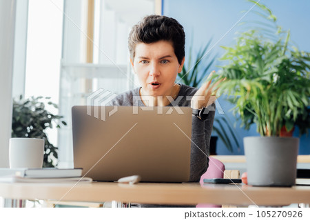 Surprized, worried middle aged neutral gender business woman having video call conference, interviewing person online, using laptop on workstation in an open space office. HR specialist, recruiting. 105270926