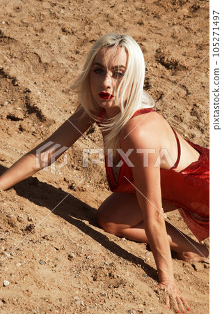Beautiful blond woman in a red sexy dress on the background of the sky and sand. Beautiful blond woman in a red sexy dress on the background of the sky and sand. 105271497