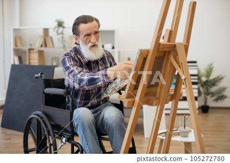 Aged man with disability painting on canvas alone at home Aged man with disability painting on canvas alone at home 105272780