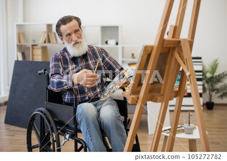 Happy retired man on wheelchair posing on camera with brush Happy retired man on wheelchair posing on camera with brush 105272782