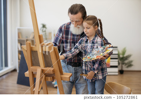 Older grandpa teaching painting to small girl indoors 105272861
