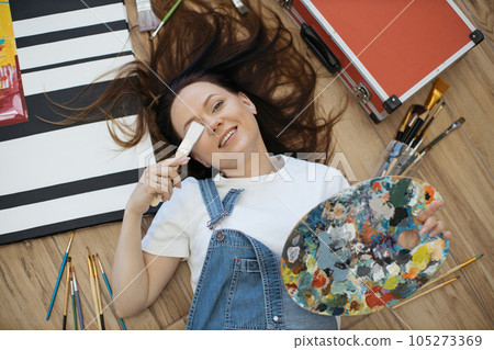 Woman with palette covering one eye with brush on floor 105273369