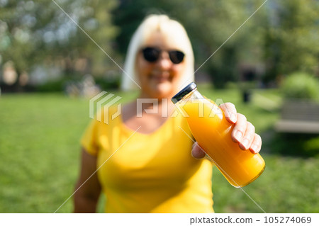 Detox diet vegetable juice concept. Attractive woman holding glass of bottle with fresh pressed orange juice at summer park 105274069