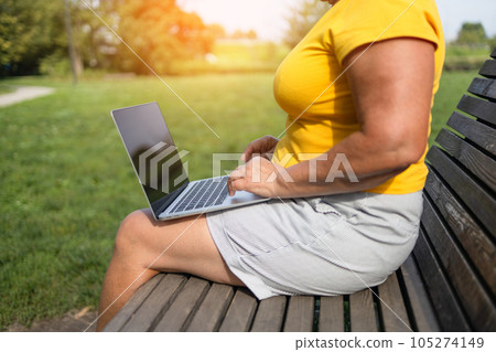 Senior blonde haired business woman using laptop computer, typing on keyboard sitting in park. Stylish freelancer, copywriter working online at workplace. Technology, successful business Senior blonde haired business woman using laptop computer, typing on keyboard sitting in park. Stylish freelancer, copywriter working online at workplace. Technology, successful business 105274149