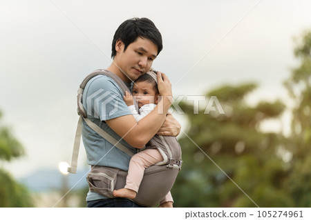 father consoling his crying infant in baby carrier in park father consoling his crying infant in baby carrier in park 105274961