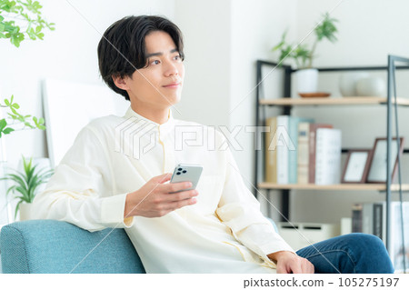 一個年輕人坐在客廳的沙發上操作智能手機 105275197