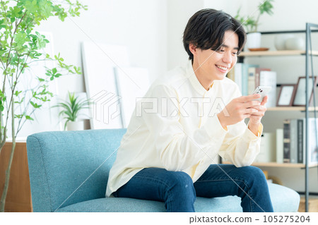 A young man sitting on a sofa in the living room and operating a smartphone 105275204