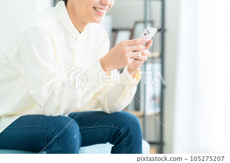 Body parts of a young man sitting on a sofa in the living room and operating a smartphone Body parts of a young man sitting on a sofa in the living room and operating a smartphone 105275207