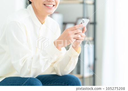 Body parts of a young man sitting on a sofa in the living room and operating a smartphone Body parts of a young man sitting on a sofa in the living room and operating a smartphone 105275208