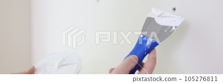 Hands with a spatula and putty near the wall, close-up 105276811