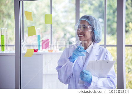 Woman scientist hand write note information in medical lab look at science microscope medical test, research biology chemistry. Asian Females technician laboratory analyzing blood test pharmaceutical 105281254