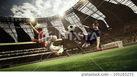 Professional female football players in motion during tense game, hitting ball, playing on 3D open air stadium. Blurred audience Professional female football players in motion during tense game, hitting ball, playing on 3D open air stadium. Blurred audience 105283255