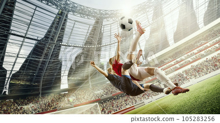 Tense game moment. Dynamic image of two women, football players in motion, hitting ball in jump during match on 3D open air stadium Tense game moment. Dynamic image of two women, football players in motion, hitting ball in jump during match on 3D open air stadium 105283256