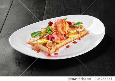 Belgian waffle with fruits, berries and vanilla ice cream, topped with caramel sauce 105285451