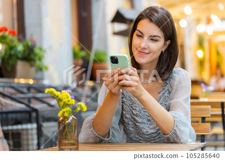 Smiling woman girl using smartphone typing text answering messages chatting online in city street Smiling woman girl using smartphone typing text answering messages chatting online in city street 105285640