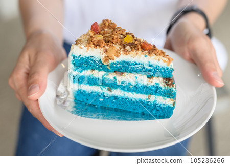Close up of someone holding a dish of Coconut cake before eating. Coconut cake is a cake frosted with a white frosting and covered in coconut flakes. 105286266