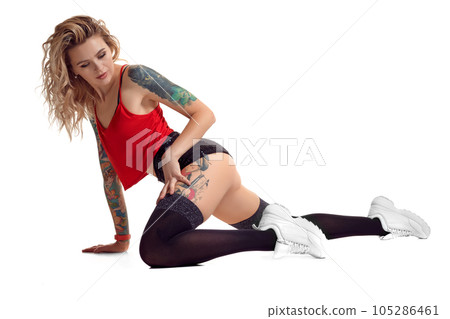 Sexy blond twerk woman with tattoed body and long curly hair is posing in studio. Sexy blond twerk woman with tattoed body and long curly hair is posing in studio. 105286461