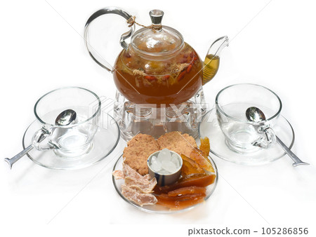 Glass tea pot with cups and crystalized fruits on white background Glass tea pot with cups and crystalized fruits on white background 105286856