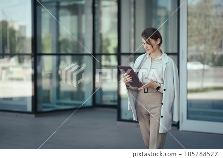 Portrait of a caucasian successful business woman used digital tablet in front of modern office building Portrait of a caucasian successful business woman used digital tablet in front of modern office building 105288527