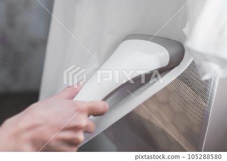 Close-up on a steamer in hand steaming white clothes on a hanger 105288580