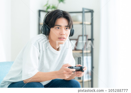 A young man sitting on a sofa in the living room and playing a game with headphones on 105288777