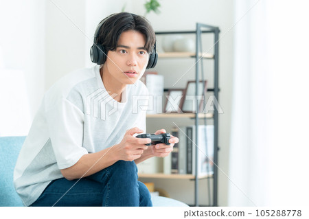 A young man sitting on a sofa in the living room and playing a game with headphones on 105288778