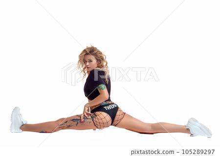Sexy blond twerk woman with tattoed body and long curly hair is posing in studio. Sexy blond twerk woman with tattoed body and long curly hair is posing in studio. 105289297