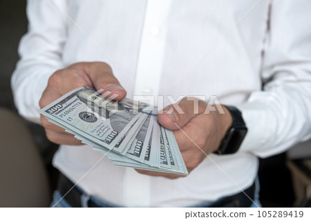 A man in a white shirt holds money, counts it and offers it to another. Close up male hand Counting and holding money us dollar. The concept of financial business and crisis. 105289419