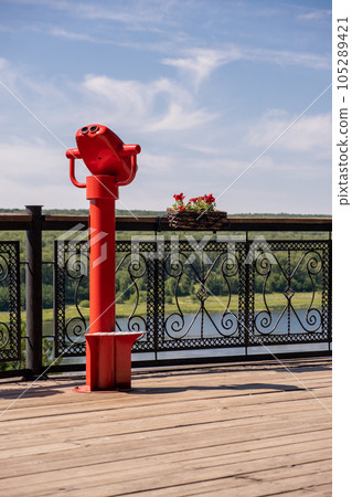 Public stationary binoculars on the banks of the river in summer or autumn to look at nature, coin-operated red metal binoculars. 105289421