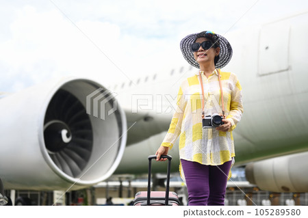 Happy 60s woman in summer clothing and sunglasses walking near the airport with a suitcase.Travel and summer vacation concept Happy 60s woman in summer clothing and sunglasses walking near the airport with a suitcase.Travel and summer vacation concept 105289580
