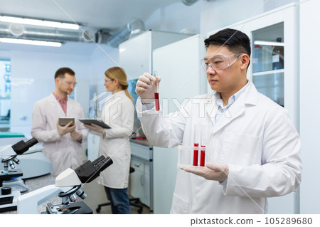 Serious asian scientist inside laboratory researching blood in test tubes, man in medical white coat. Serious asian scientist inside laboratory researching blood in test tubes, man in medical white coat. 105289680