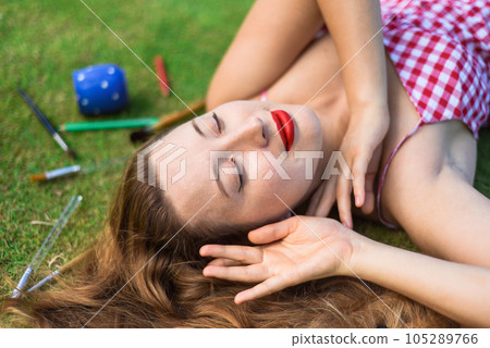 Beautiful woman artist and illustrator laying on the lawn with dropped easel, drawings, pencils Beautiful woman artist and illustrator laying on the lawn with dropped easel, drawings, pencils 105289766