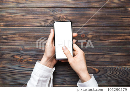 Top view of woman hands holding smart phone with blank copy space screen for your text message or information content. woman hand using phone white screen on top view Top view of woman hands holding smart phone with blank copy space screen for your text message or information content. woman hand using phone white screen on top view 105290279