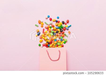 shopping paper gift bag in corner full of assorted traditional candies falling out on colored background with copy space. Happy Holidays sale concept 105290633
