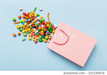 shopping paper gift bag in corner full of assorted traditional candies falling out on colored background with copy space. Happy Holidays sale concept shopping paper gift bag in corner full of assorted traditional candies falling out on colored background with copy space. Happy Holidays sale concept 105290638