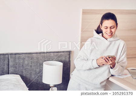 A happy woman checks social networks while holding a smartphone at home. Smiling young woman using a mobile phone app, playing games, shopping online, ordering delivery. High quality photo A happy woman checks social networks while holding a smartphone at home. Smiling young woman using a mobile phone app, playing games, shopping online, ordering delivery. High quality photo 105291370