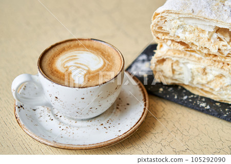 Breakfast in the cafe, morning coffee. Cappuccino and dessert Napoleon on the table. 105292090