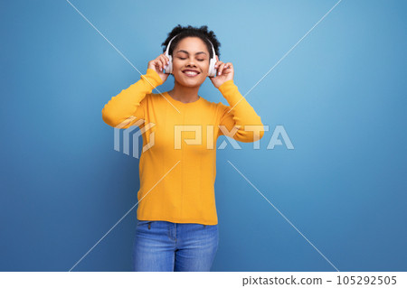 young latin woman with afro hair listening to music with headphones on studio background 105292505