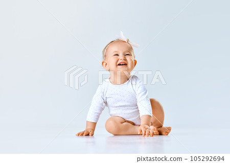 Portrait of cheerful little baby girl, toddler, child calmly sitting and laughing against grey studio background Portrait of cheerful little baby girl, toddler, child calmly sitting and laughing against grey studio background 105292694