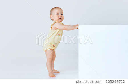 Adorable little baby girl, child, toddler in comfortable cute clothes standing and looking against grey studio background Adorable little baby girl, child, toddler in comfortable cute clothes standing and looking against grey studio background 105292712