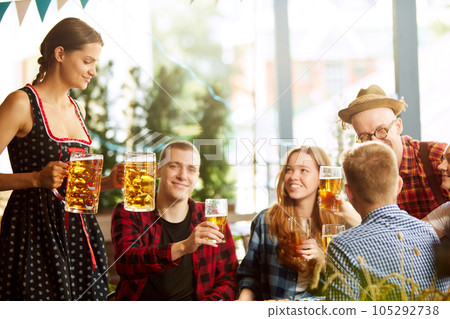 Beautiful young woman, waitress serving big mugs with lager beer to group of young people, friends meeting together at pub Beautiful young woman, waitress serving big mugs with lager beer to group of young people, friends meeting together at pub 105292738