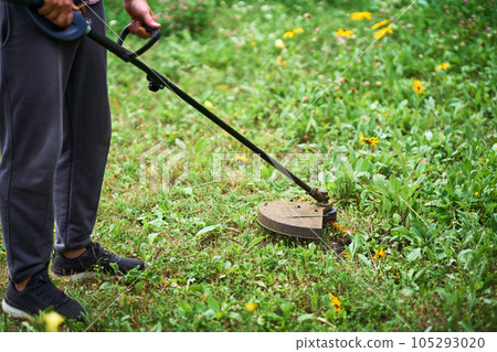 Close up of young man cutting grass with weed cutter on his grassy lawn. Close up of young man cutting grass with weed cutter on his grassy lawn. 105293020