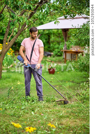 Young man cutting grass with weed cutter on his grassy lawn. Young man cutting grass with weed cutter on his grassy lawn. 105293044