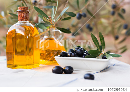 Black ripe olives, olive oil in a glass traditional bottle on table in an olive garden Black ripe olives, olive oil in a glass traditional bottle on table in an olive garden 105294984